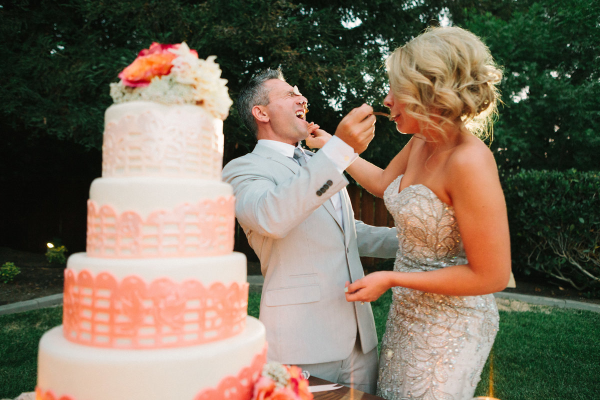 Bride and groom smash cake in each others faces at wedding reception