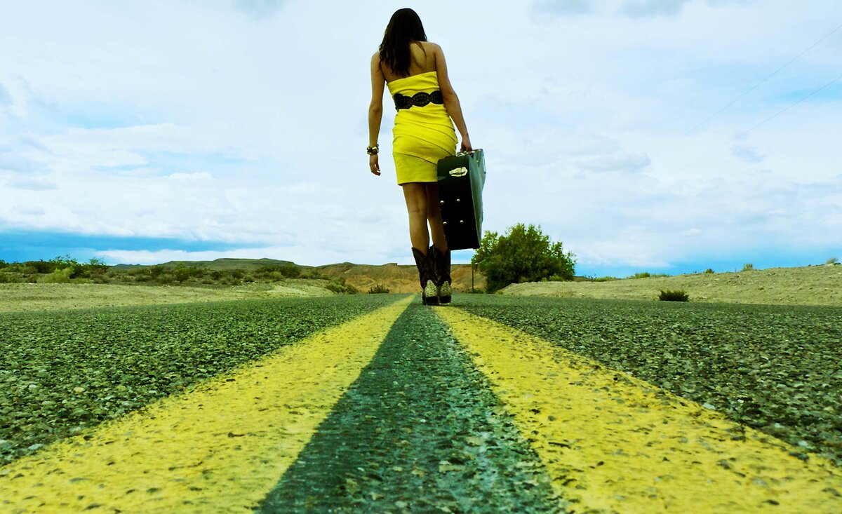 Female musician portrait Leanne Pearson wearing yellow dress caring guitar case down middle yellow road lines
