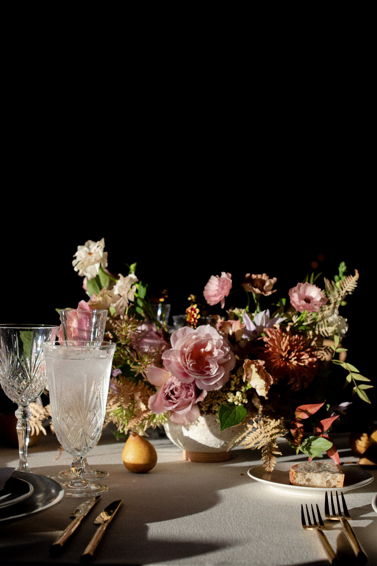 Dramatic wedding tablescape with waterford crystal glasses, brown pears, and a creative pink, brown, and green floral centerpiece.