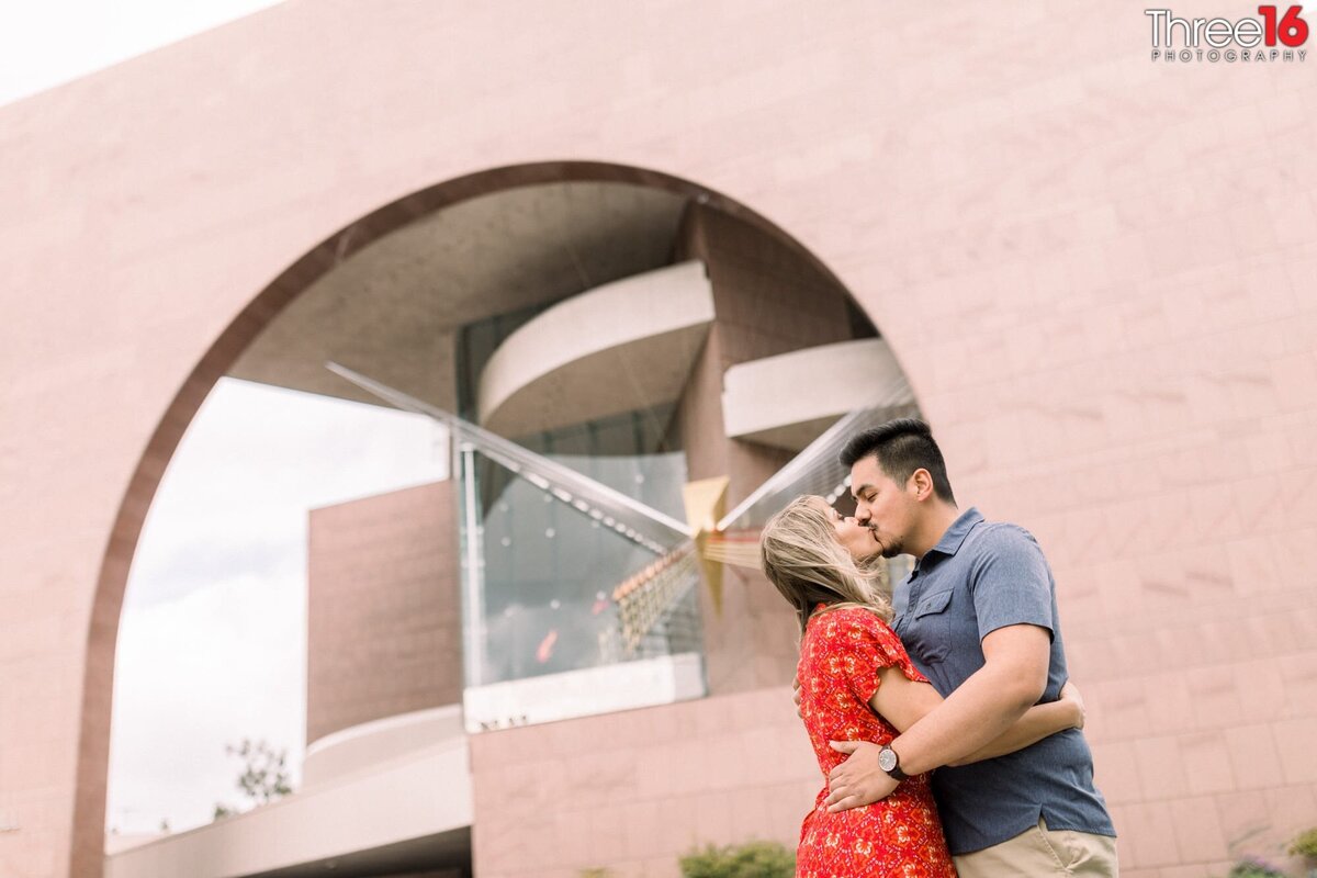 Engaged couple share a kiss in front of some unique architecture at the Segerstrom Center for the Art