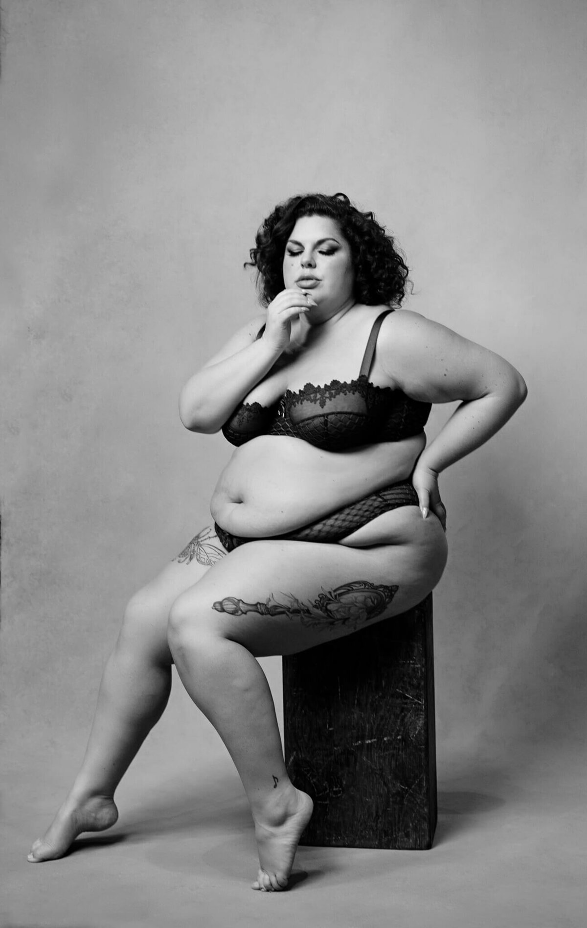plus size woman is posing very sexy while seated in a photography boudoir studio