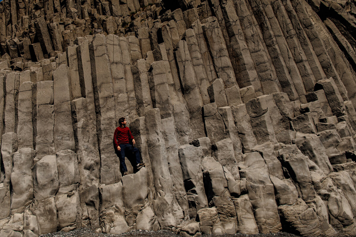 Environmental portrait of man in red sweater standing on rock formations at Reynisfjara black beach in Iceland