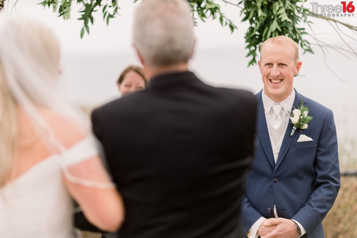 Groom stands at the altar smiling as his Bride arrives on her dad's arm