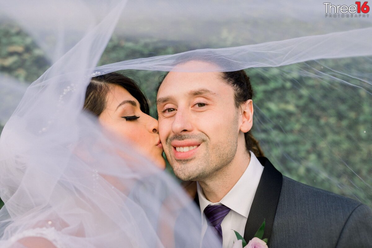 Bride kisses her Groom on the cheek under her veil