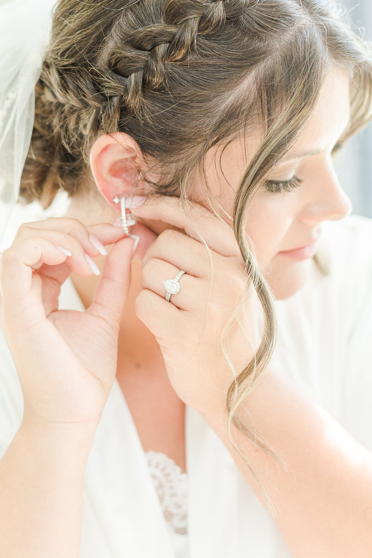 Bride's getting ready image. The bride is captured putting on her earring with her engagement ring featured. Captured by Lia Rose Weddings