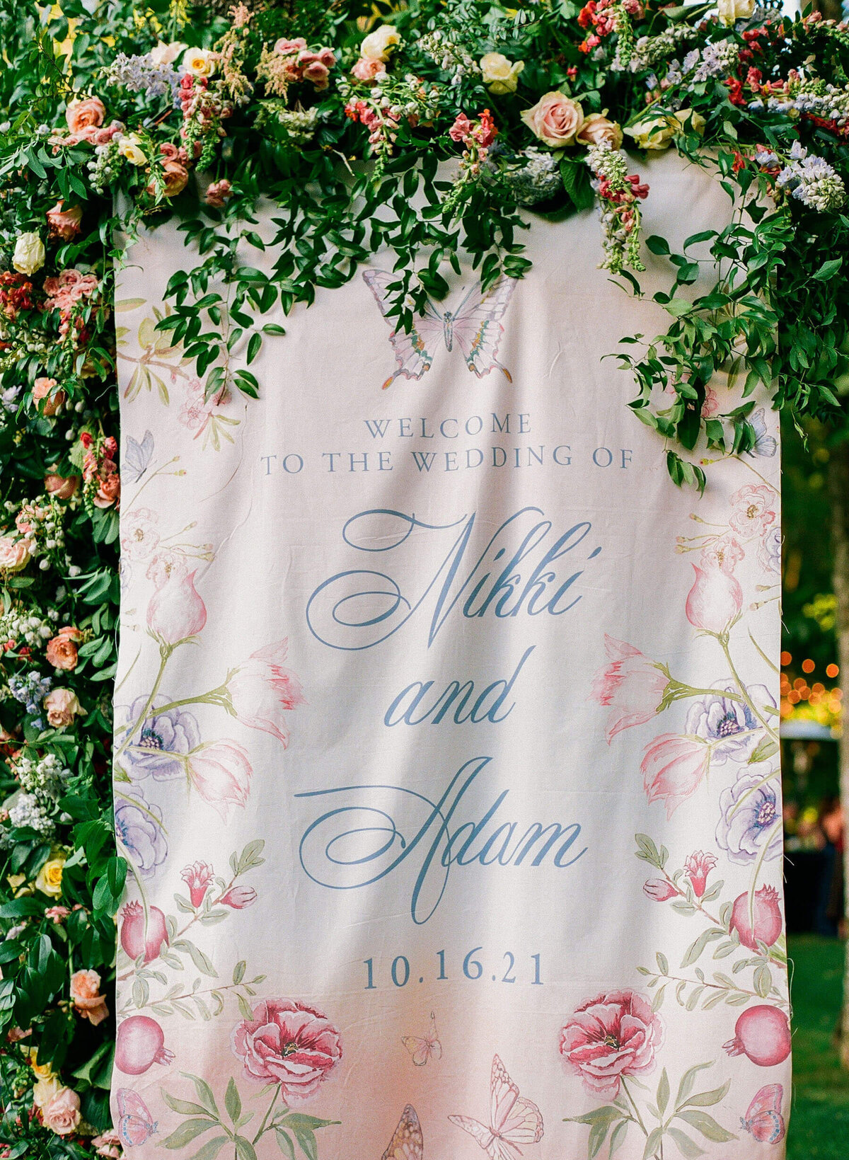 Printed Welcome sign hanging in tree surrounded with fresh pastel flowers.