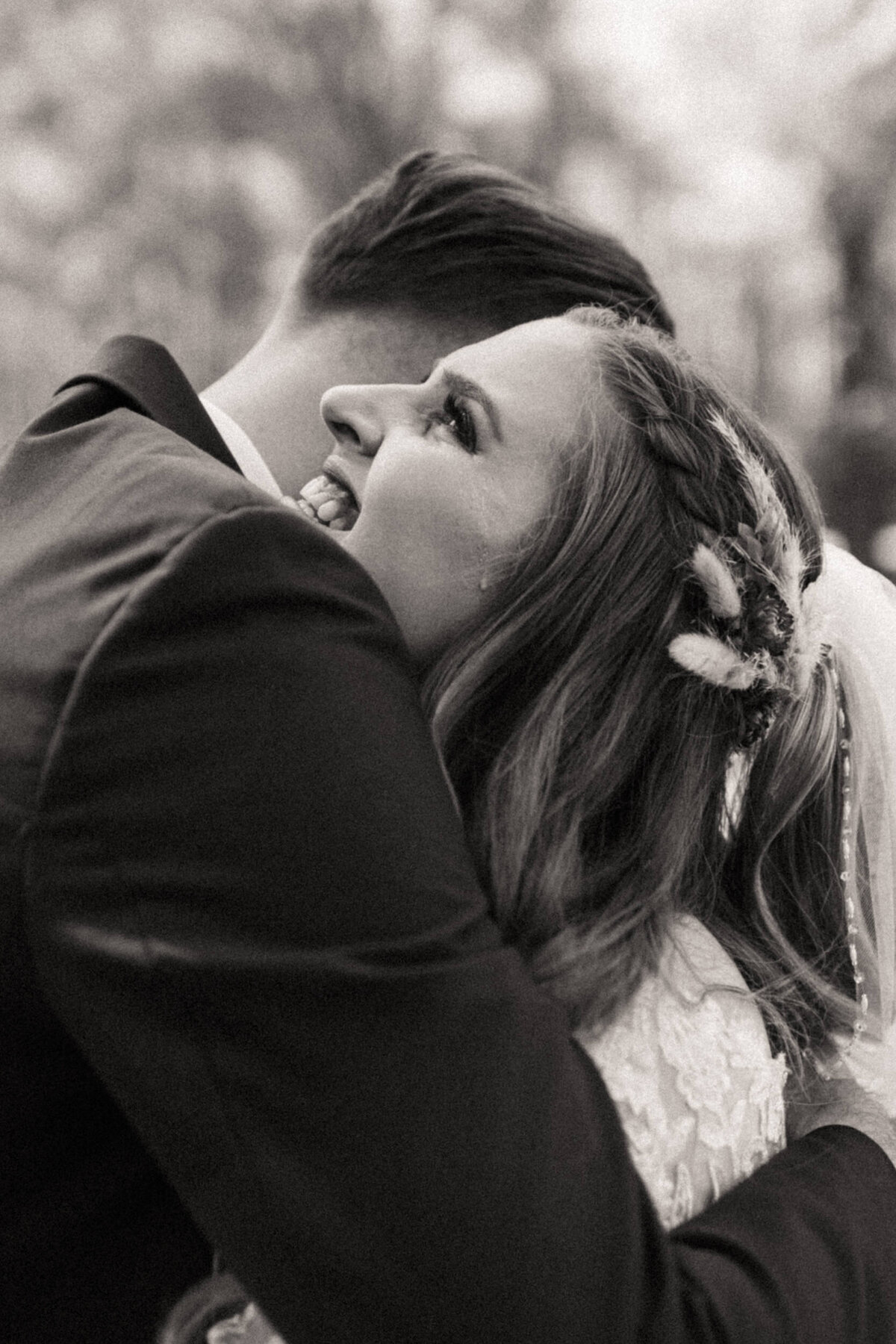 Emotional bride has a tear running down her cheek as she smiles and embraces a hug from her groom during their first look