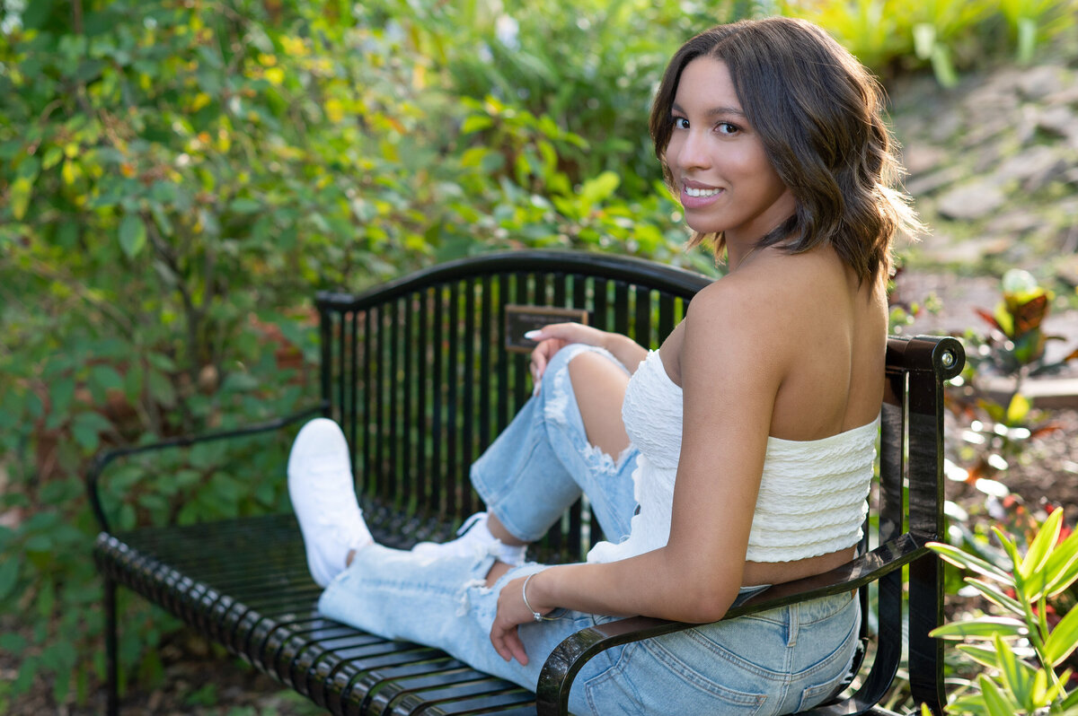 High school senior girl in casual clothing sits stretched across a bench.