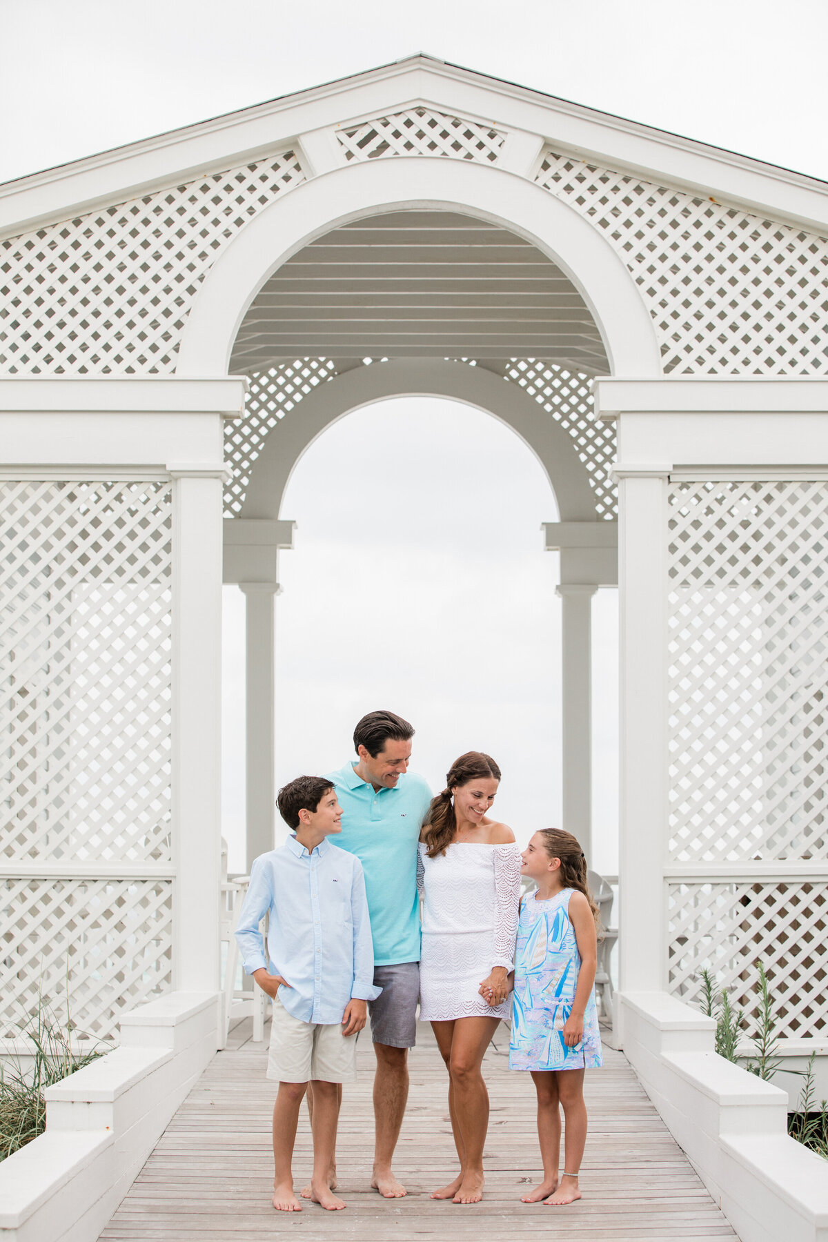 A family of four standing on a small pier smiling at each other.