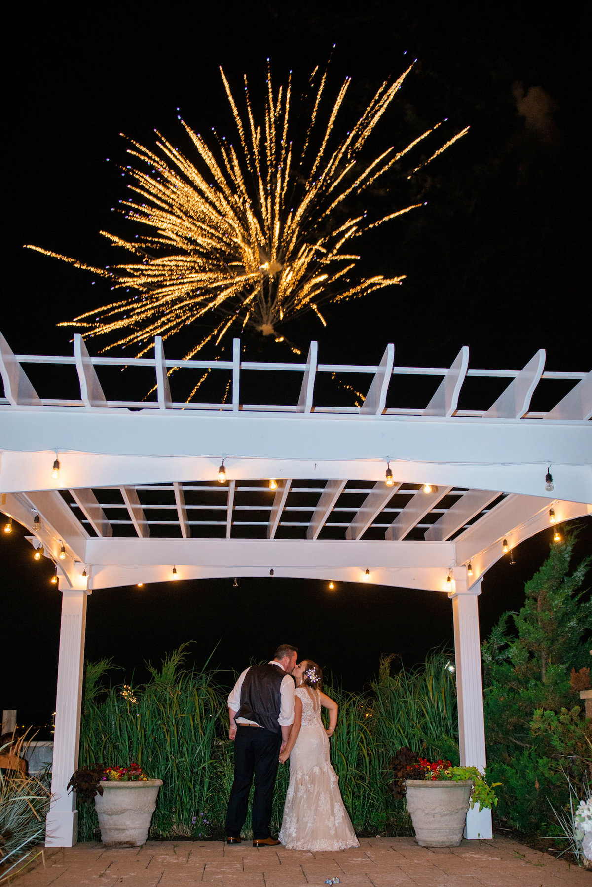 bride and groom kissing during outdoor wedding reception with fireworks at Lombardi's on the Bay