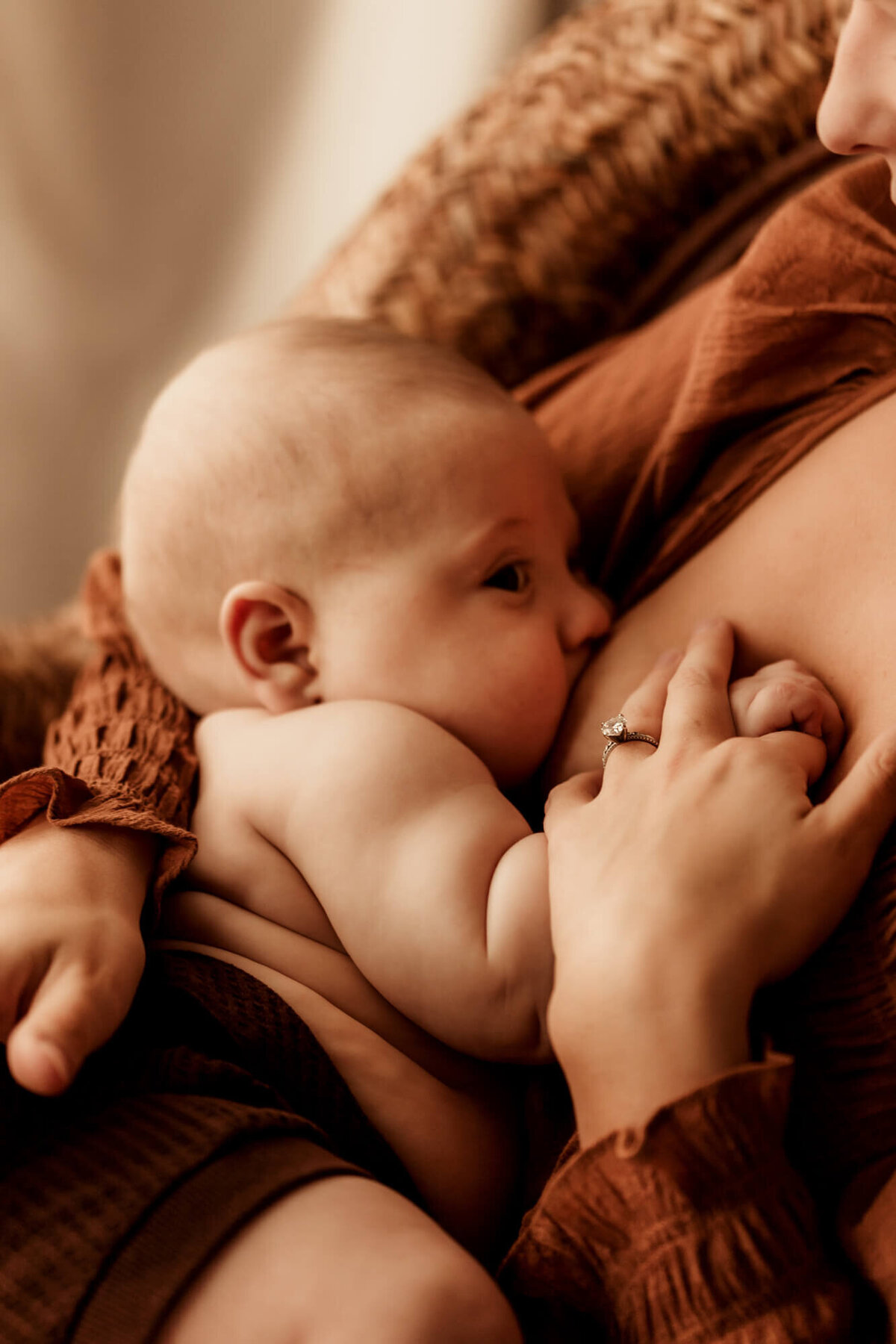 Baby boy nursing holds his mother's hand.