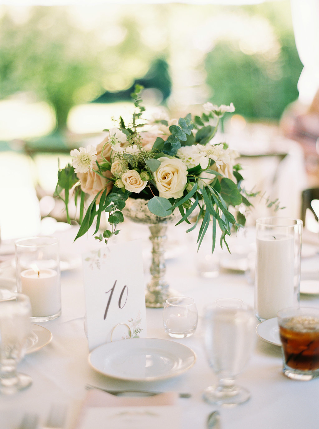 Silver compote arrangements with roses and spiral eucalyptus are perfect on the round tables at this wedding reception.