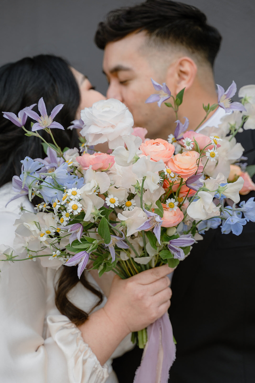 Bride holding a pastel bouquet while kissing her groom