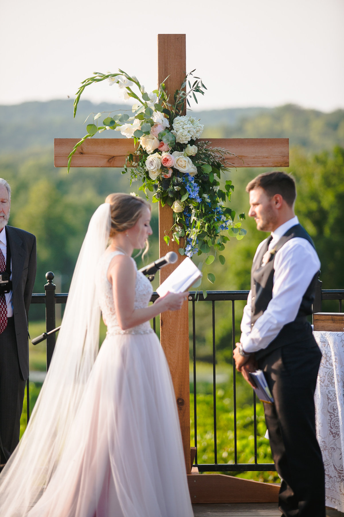 Bride and groom exchange vows in front of a wooden cross at Vineyard at Chandler Hill.