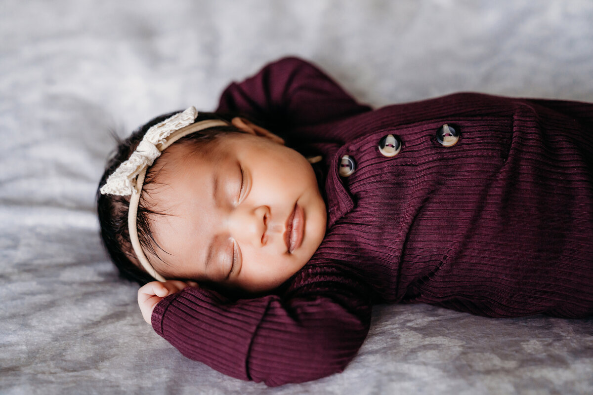 Newborn Photographer, a baby girl lays sleeping on bed with headband on her head