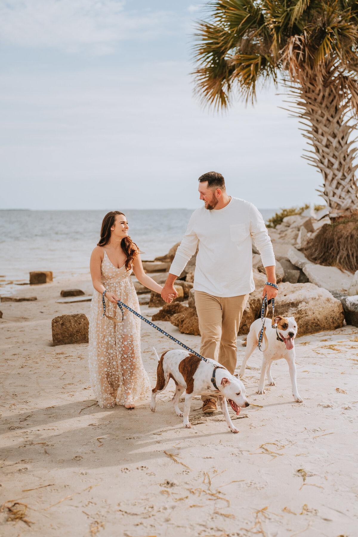 man and woman smiling at each other while walking on the beach with their dogs in tarpon springs florida