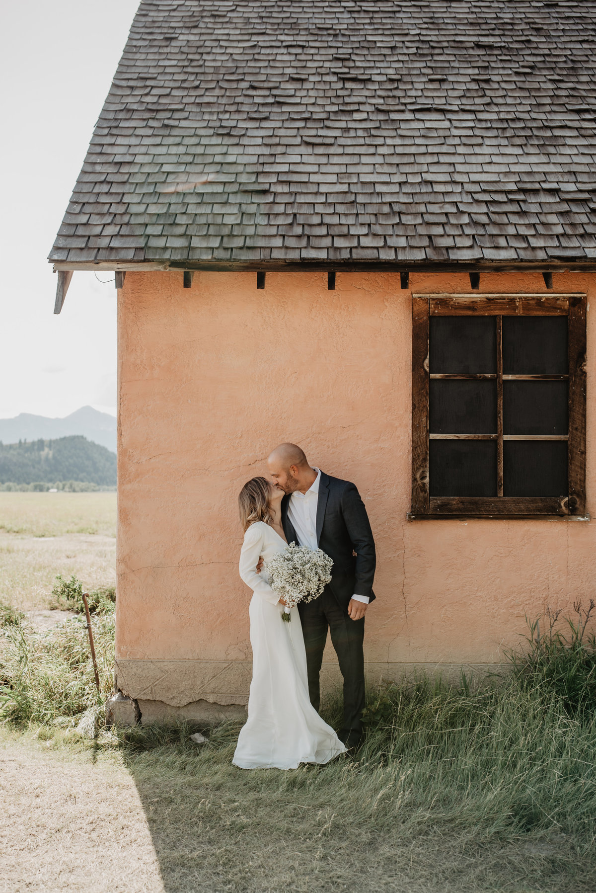 jackson wyoming photographer captures outdoor bridals with Bride and groom in the Tetons to elope, are standing in front of a stucco house with rustic details