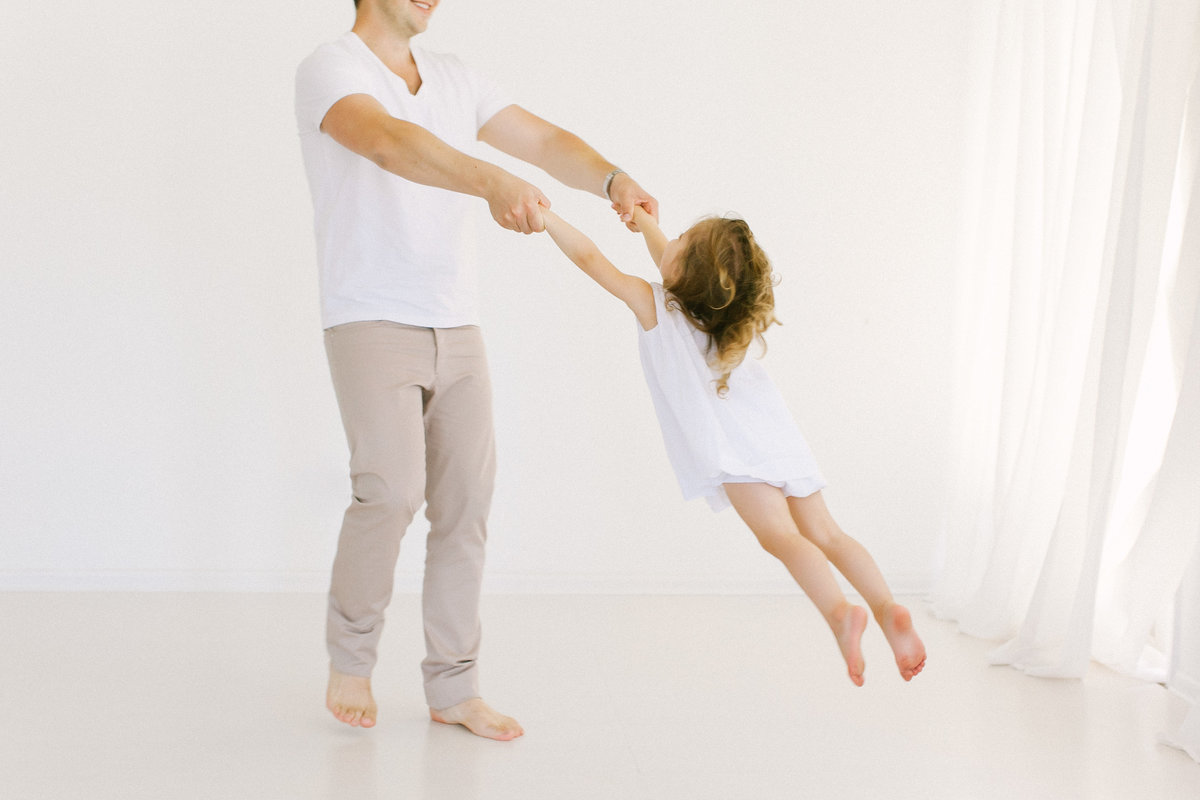 Father dancing and twirling his daughter in Laurie Baker's white studio