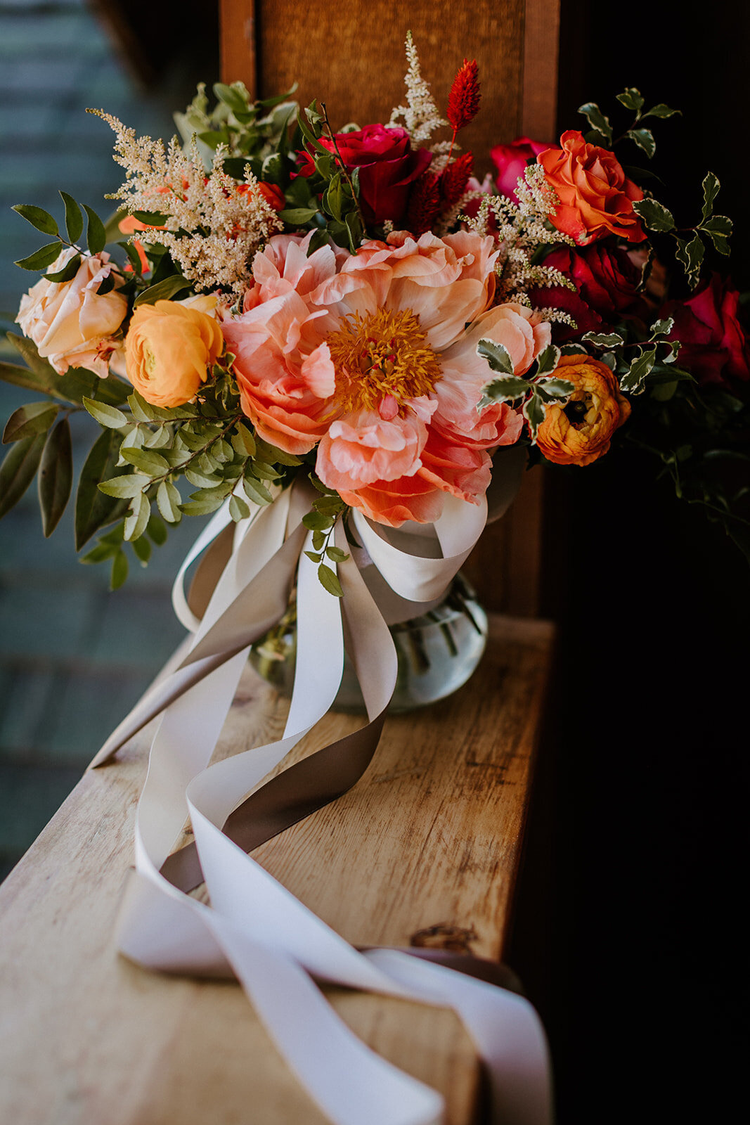 Vibrant wedding bouquet with peony and ranunculus tied with long ribbons on a wooden table in Sisters Oregon
