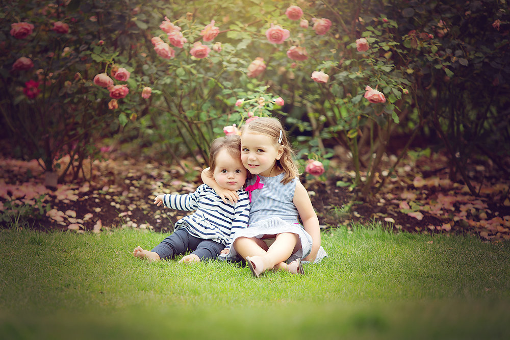 little sisters sitting under rose bush