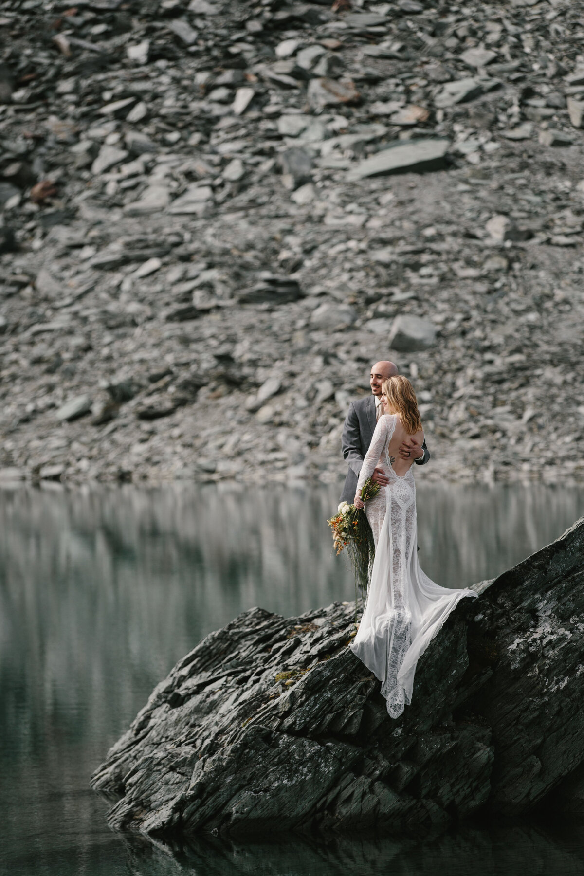 The Lovers Elopement Co - bride and groom together on rock next to lake with reflections - destination wedding Queenstown