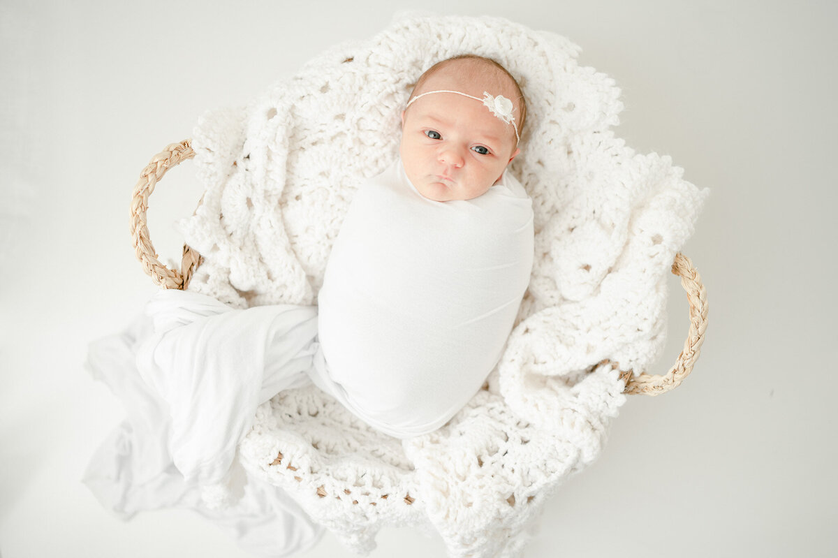 newborn swaddled in white lays in a basket In Kristie Lloyd’s Nashville newborn photographer studio