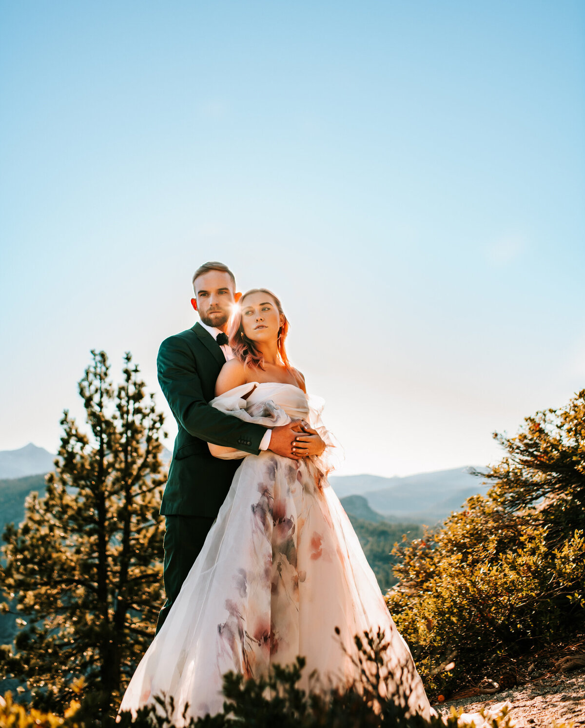 Couples Photography, man in a blazer wraps his arms around woman in a wedding dress in front of the mountains