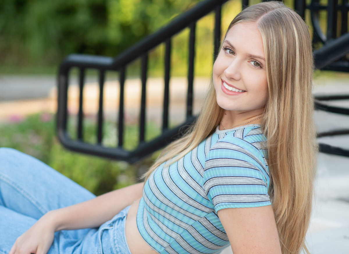 High school senior girl in casual clothing leans across stairs smiling at camera.