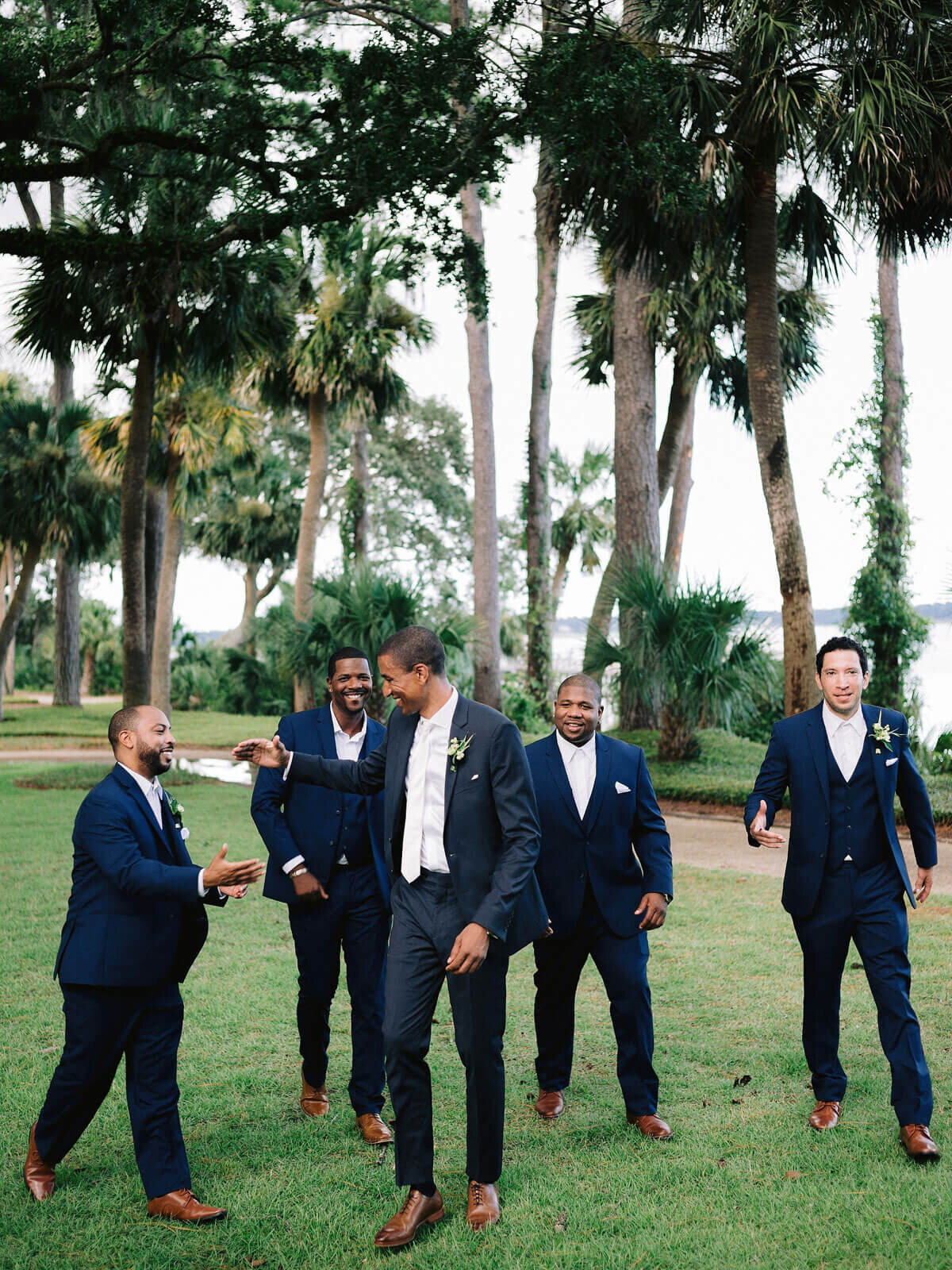 The groom and groomsmen are happily walking in the beautiful garden of Montage at Palmetto Bluff. Destination wedding image by Jenny Fu Studio