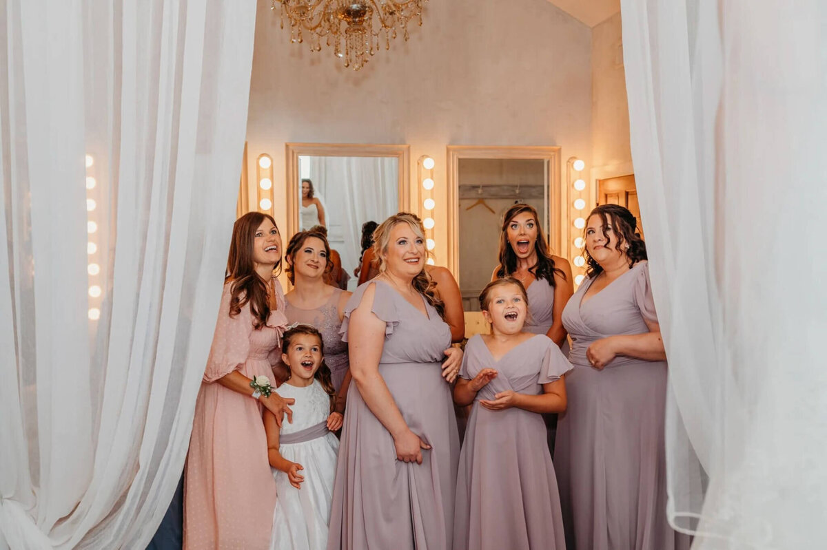 photo of bridesmaids wearing lavender and smiling and all during their first look with the bride inside of a white building