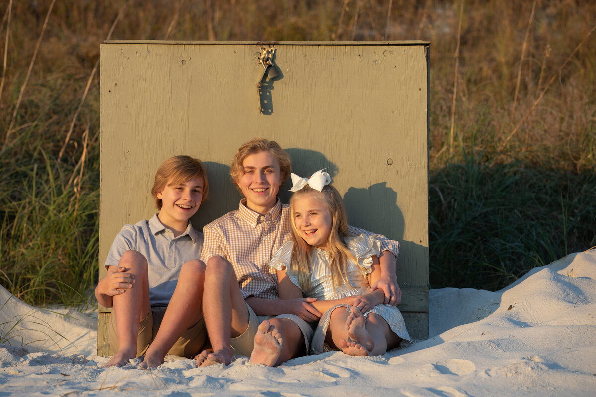 Three siblings sitting in the sand together