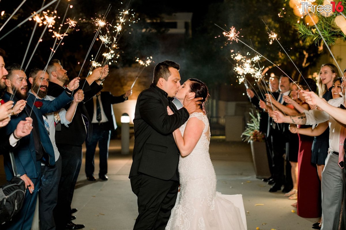 Bride and Groom stop for a kiss while walking under the human tunnel of sparklers