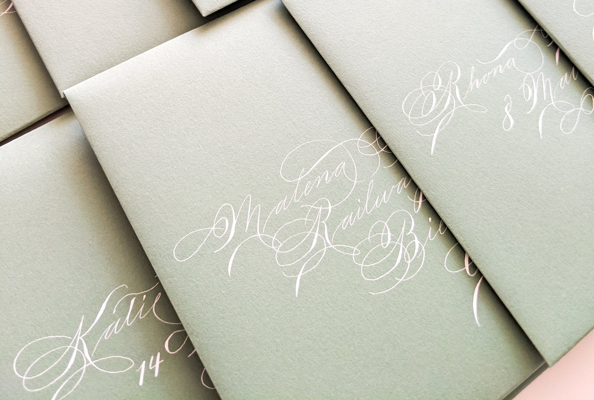 Spencerian envelope calligraphy with white ink on light green envelopes