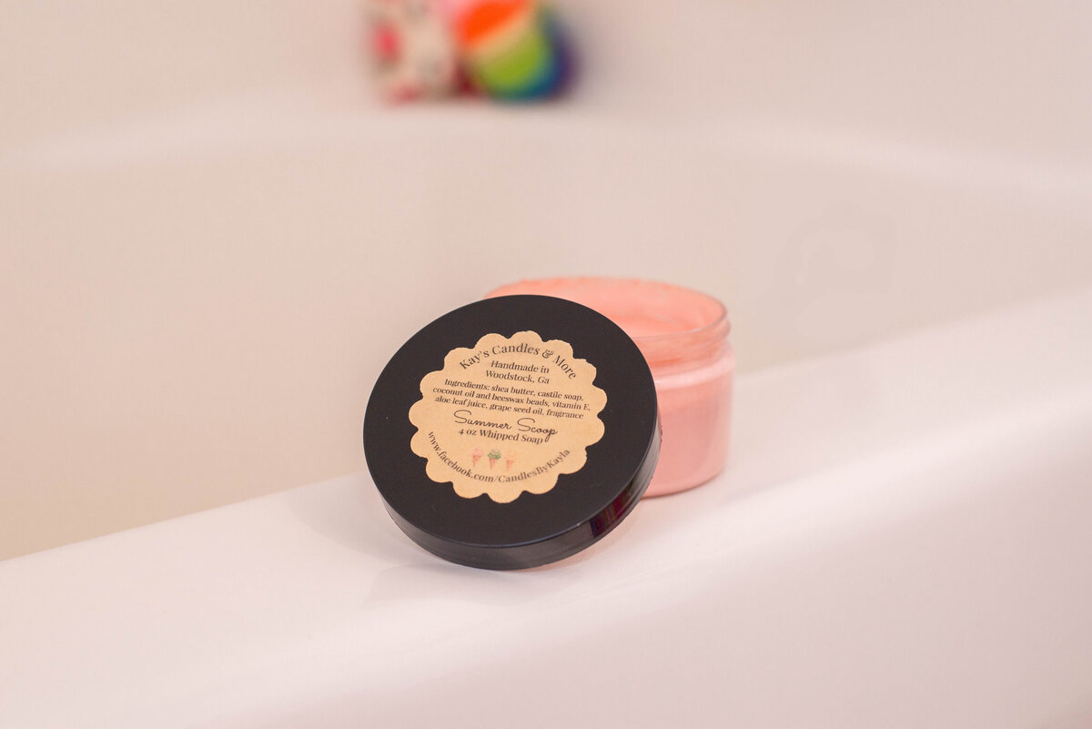 A jar of pink cosmetic cream on a bathroom counter with soft focus background featuring colorful objects.