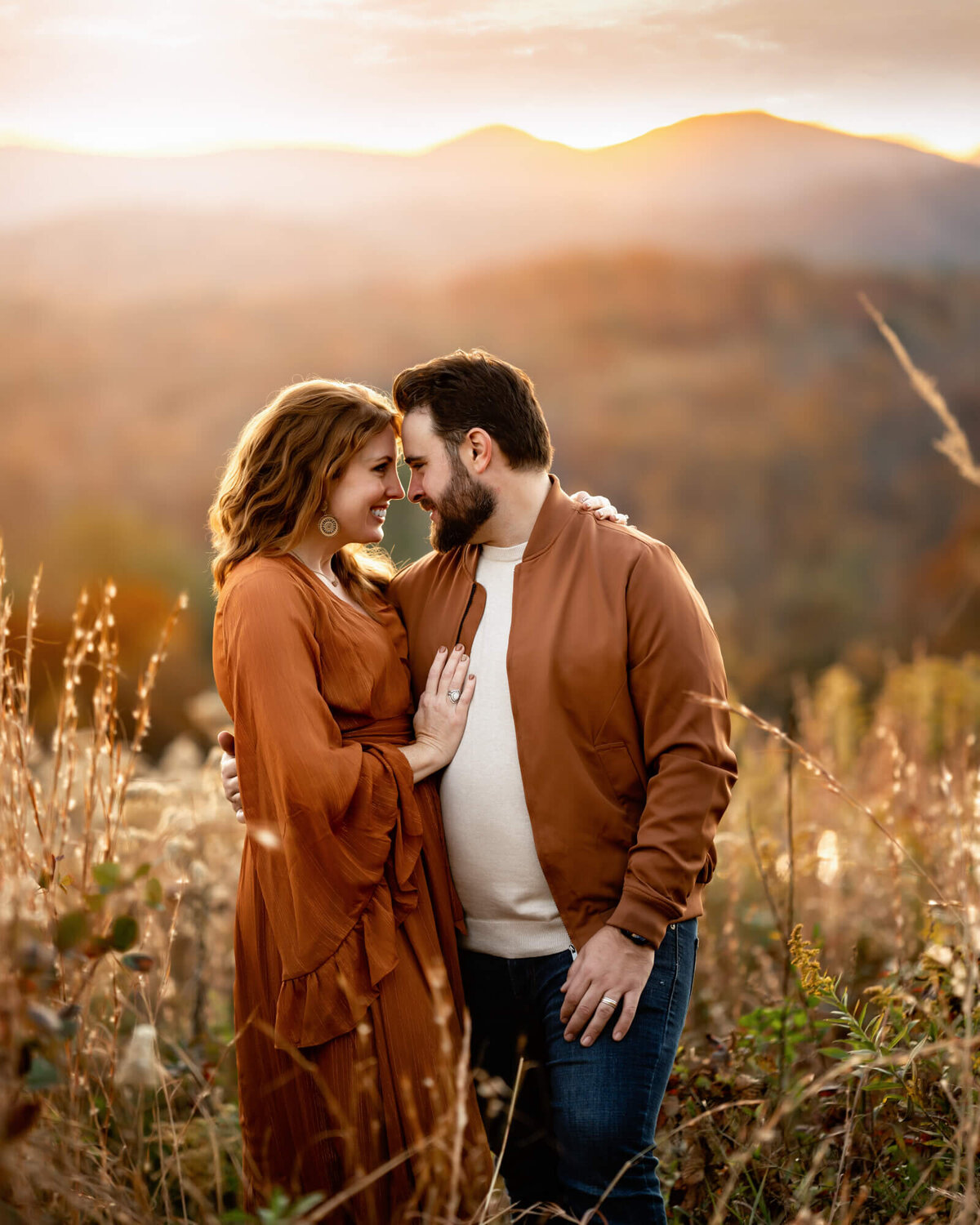 A couple dressed in fall colors touching foreheads and laughing during a photo session with an Asheville Family Photographer