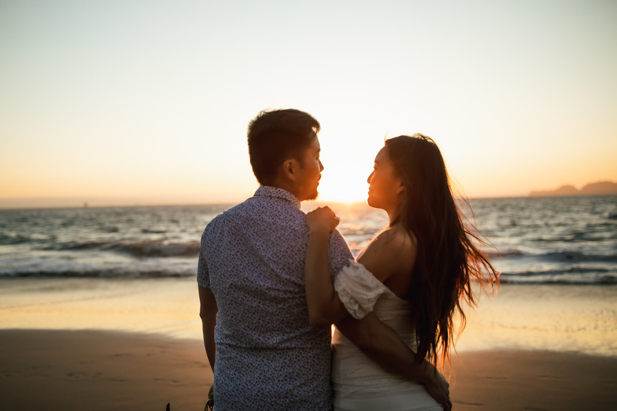 Bay Area couple look at each other while embraced at sunset photography session on SF Baker Beach