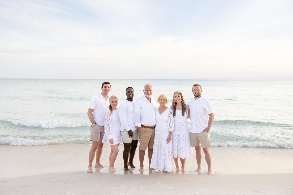 A family in white standing together smiling on the beach near 30A.