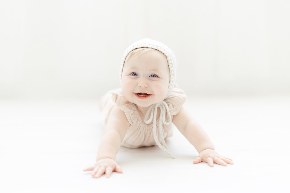 A baby girl on the floor crawling around a photography studio for her baby pictures.