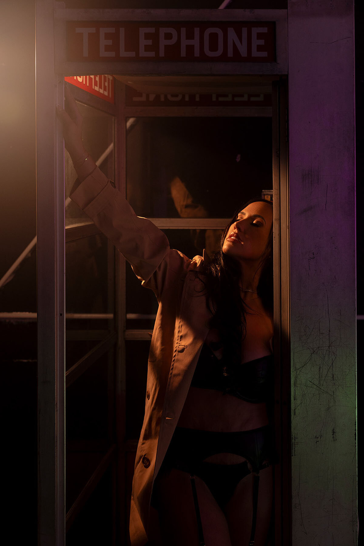 Darkly lit artistic boudoir portrait of woman in phone booth