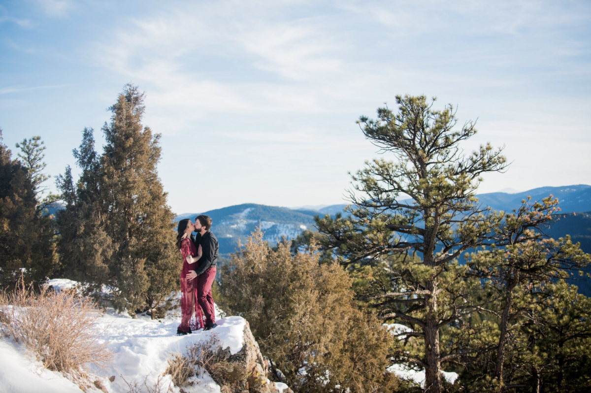 A wide angle shot of a man and woman standing on a snowy overlook ledge