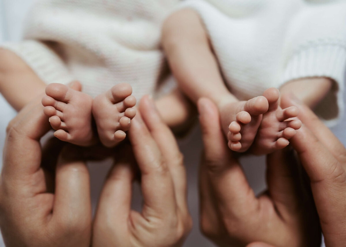 Two pairs of the sweetest little toes being held together by their parents.