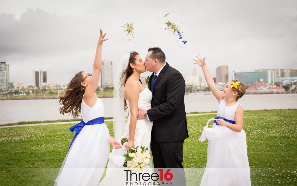 Flower Girls toss flower pedals in the air as couple kisses