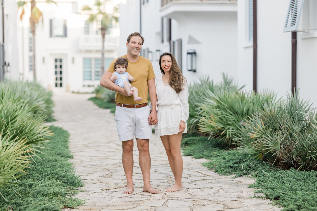 A dad holding a baby in one hand and his partner's hand in the other near South Charles Street in Alys Beach.