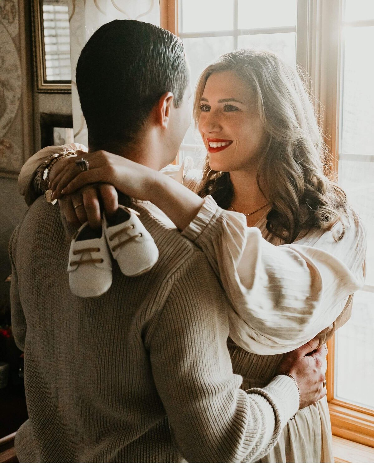 A maternity photographer in Pittsburgh capturing a couple embracing by a window.