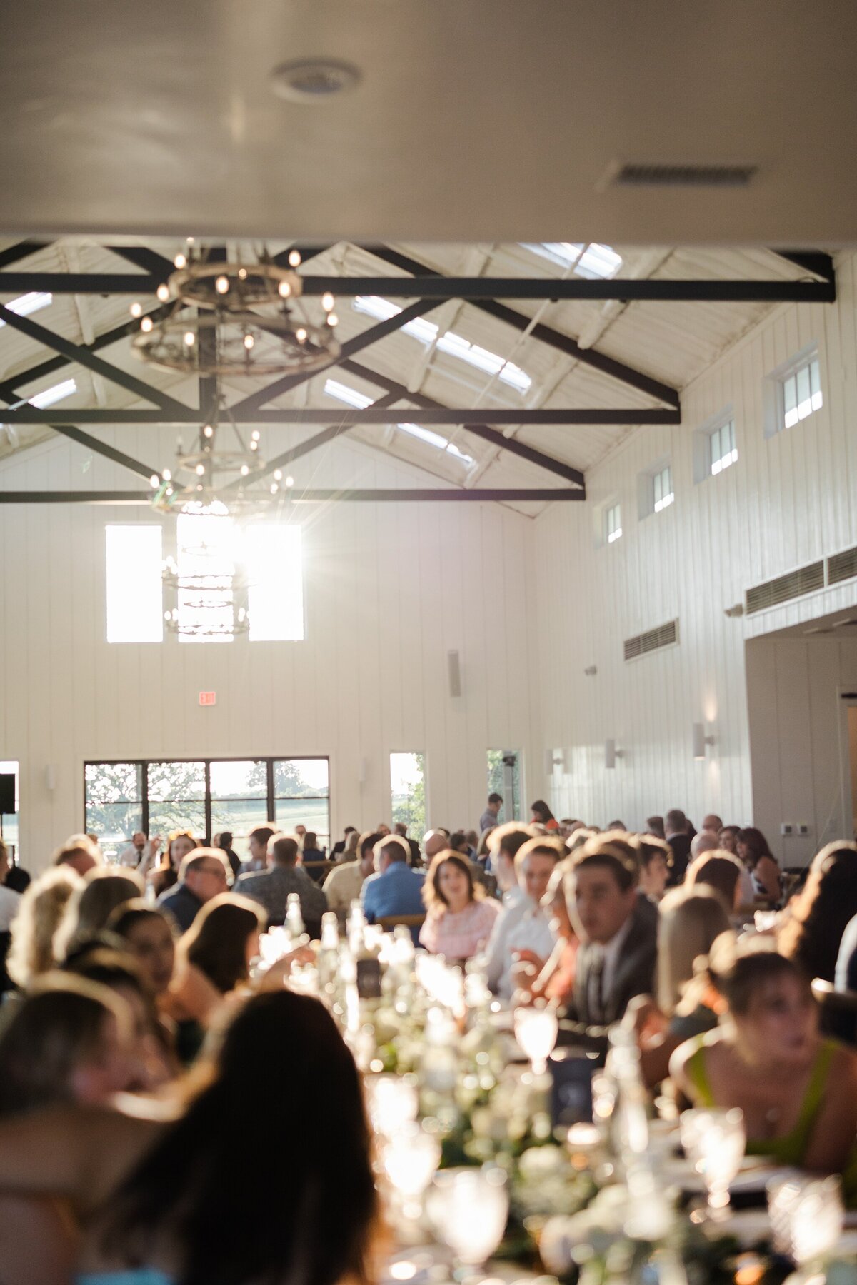 A candid shot of all the wedding guests at a wedding reception at Bella Cavalli Events in Aubrey, Texas.  Guests can be seen at many tables all socializing and preparing to eat dinner and celebrate the couple and their day.