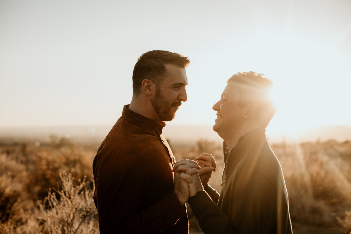 two men holding hands in the desert with sun flare