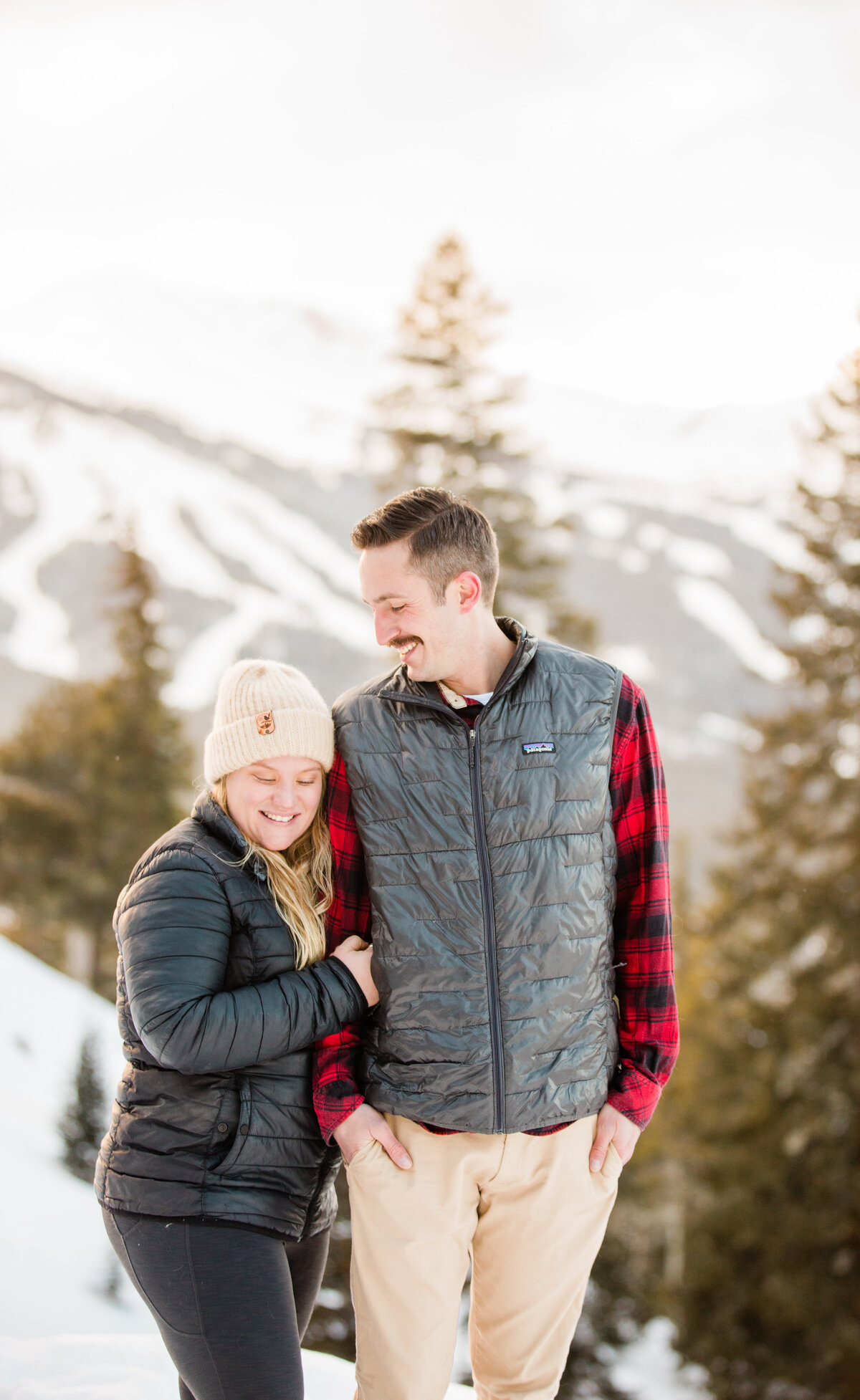 A man is gazing at his fiance  as she smiles and looks down. Breckenridge Ski resort is behind them