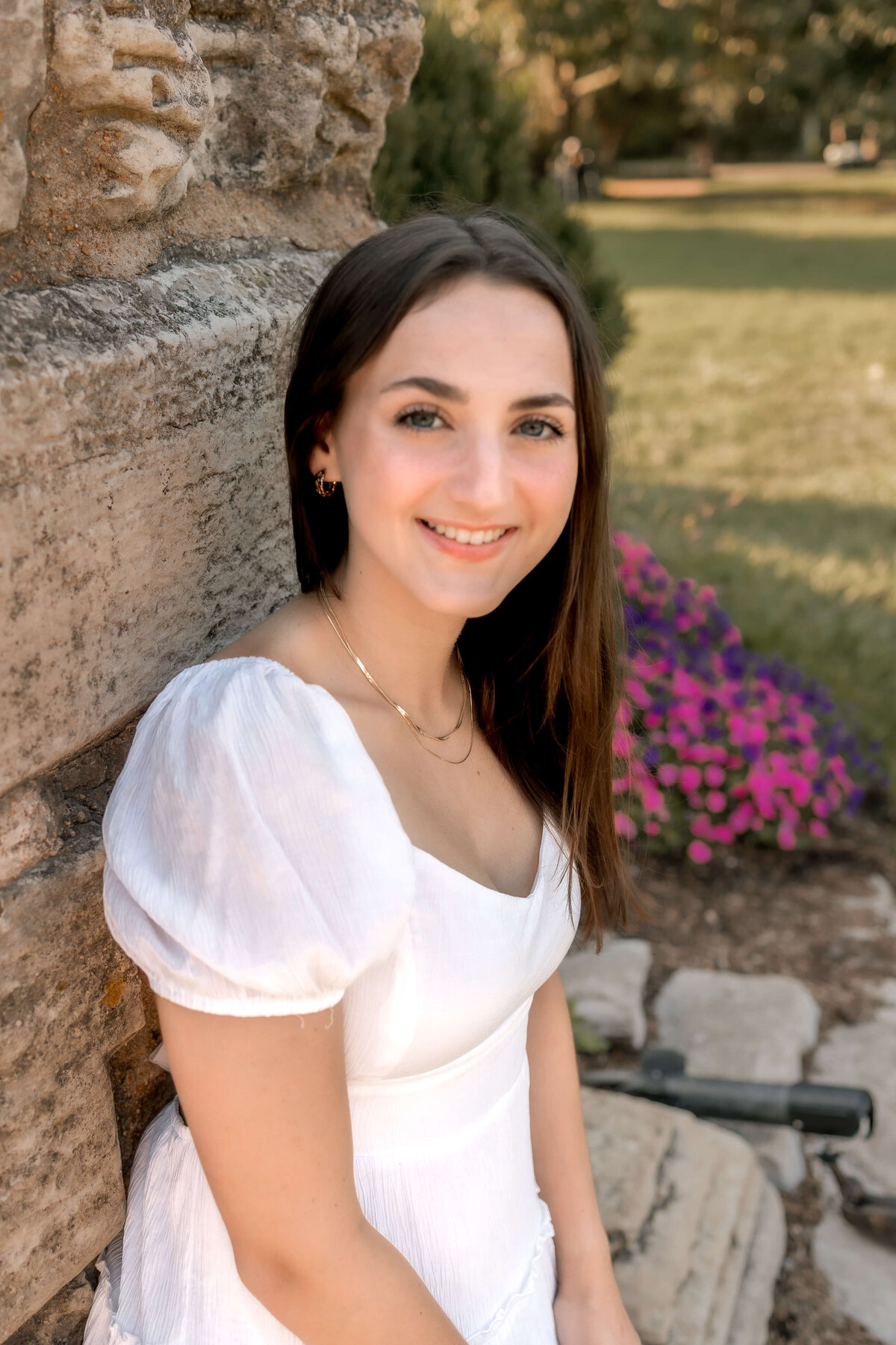 beautiful brown haired girl posing for her senior photos at tower grove park, leaning against a stone wall.