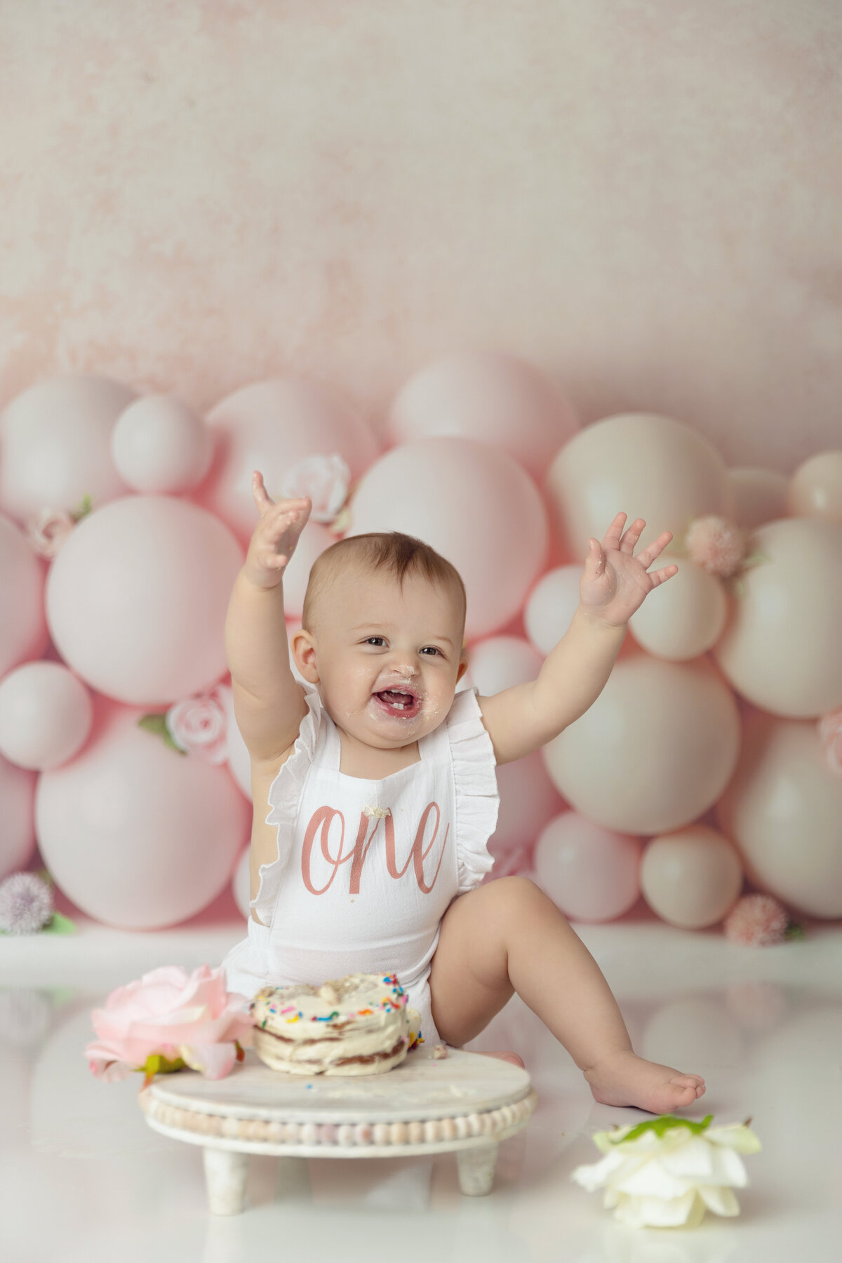 A happy little girl in a "one" onesie celebrates her first birthday with a New Jersey Cake Smash Photographer