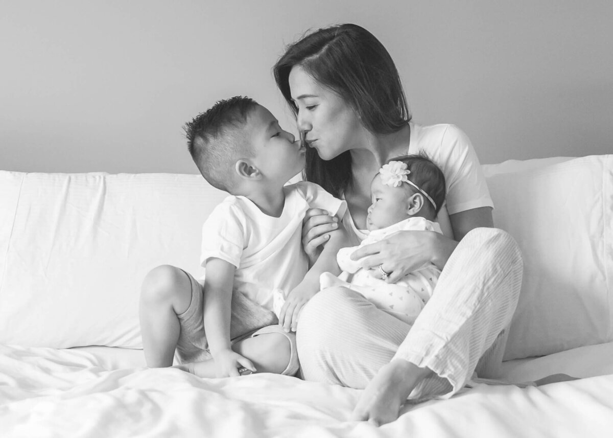 light and airy black and white photo of mother son and baby in master bed, embracing